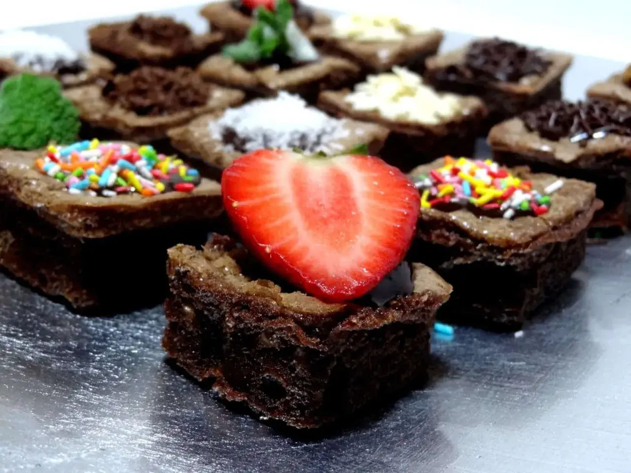 Deliciosos brownie sin huevo, decorados con fresa, chispas de colores, coco rallado y virutas de chocolate.