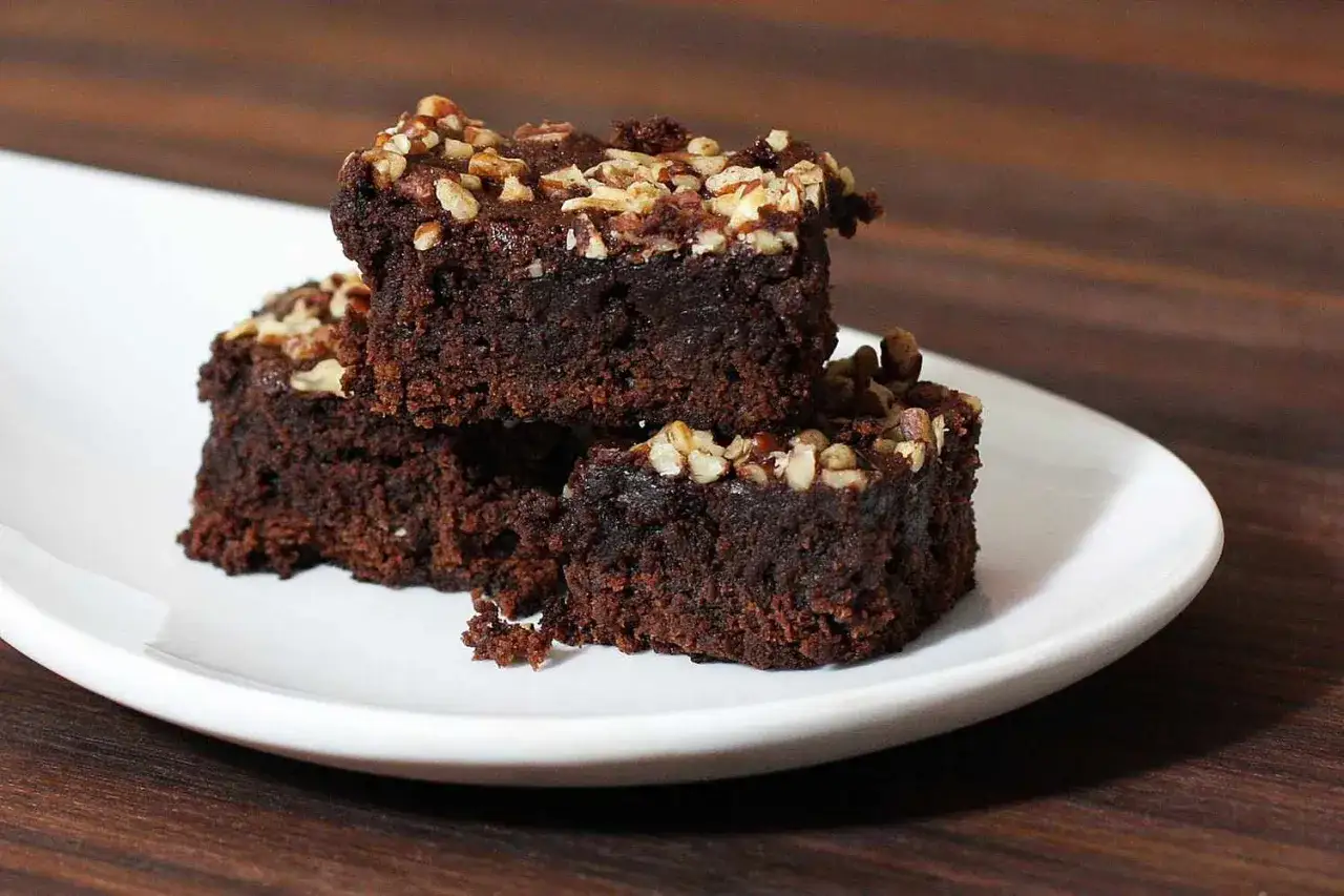 Tres trozos de brownie sin horno, cubiertos con nueces picadas, apilados en un plato blanco.