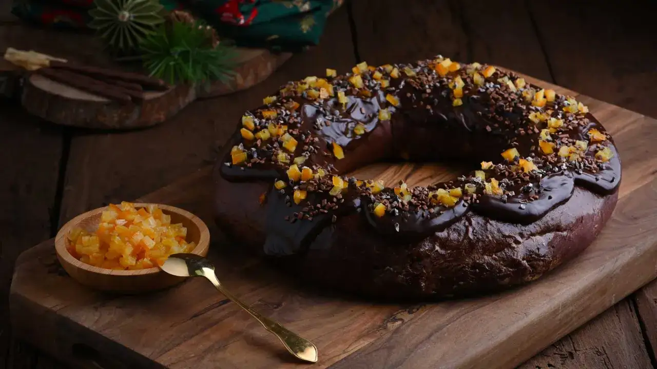 Delicioso roscon de reyes chocolate, cubierto con glaseado oscuro y trocitos de naranja confitada.