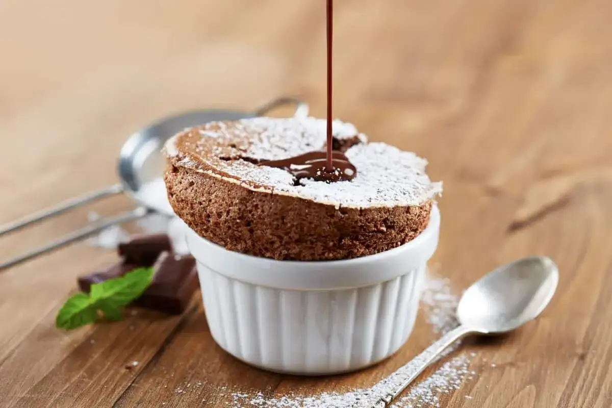 Delicioso souffle de chocolate, cubierto de azúcar glas, con sirope de chocolate cayendo.