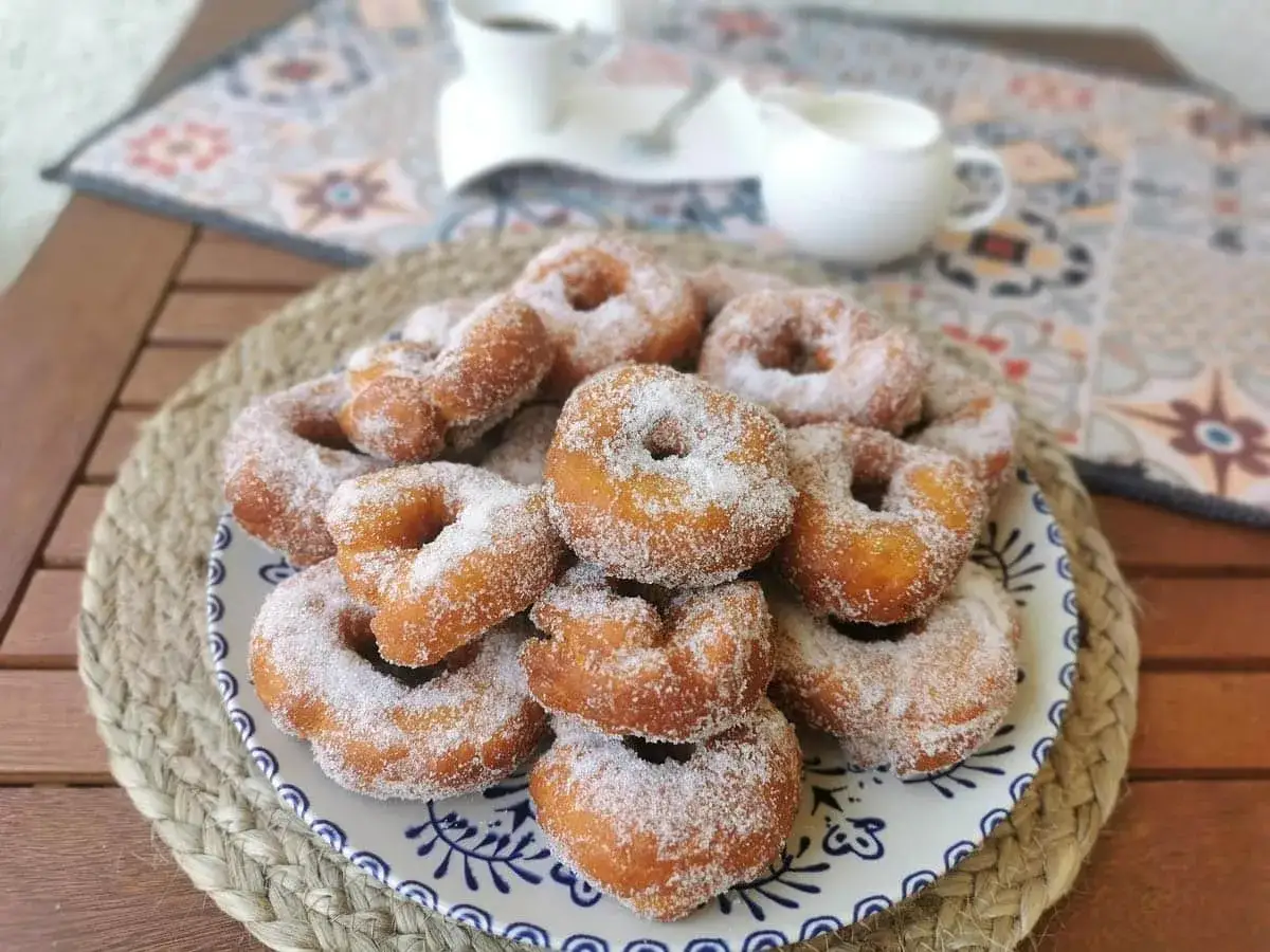 Un plato lleno de rosquillas de anís recién hechas, cubiertas de azúcar. Perfectas para acompañar un café.