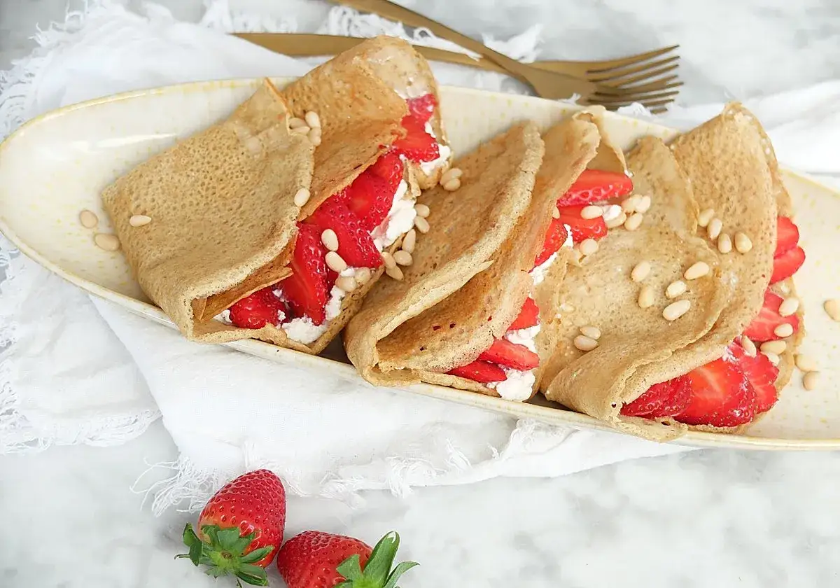 Deliciosos crepes con harina de almendras, rellenos de fresas frescas y queso crema, espolvoreados con piñones.