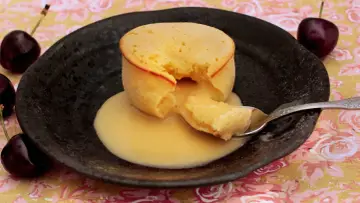 Coulant de chocolate blanco con interior cremoso, servido en plato negro con cerezas.