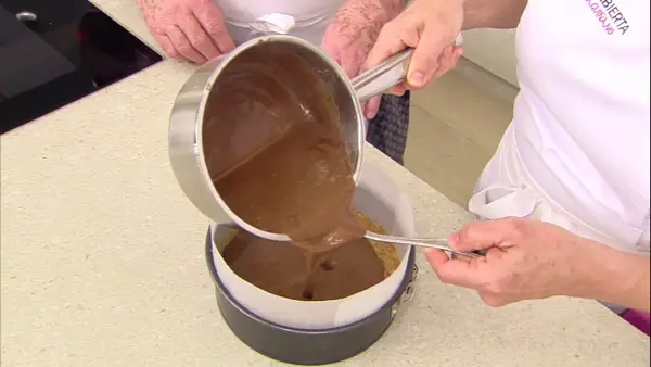 Vertiendo cobertura de chocolate sobre una base de galleta para un delicioso pastel de chocolate.
