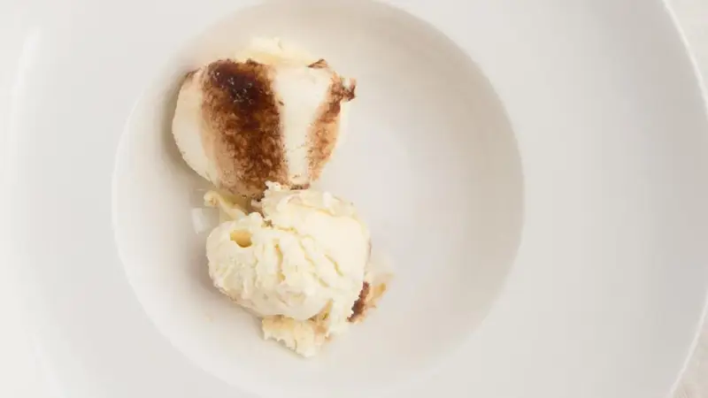 Dos bolas de helado de tiramisú con un toque de cacao en polvo en un cuenco blanco.