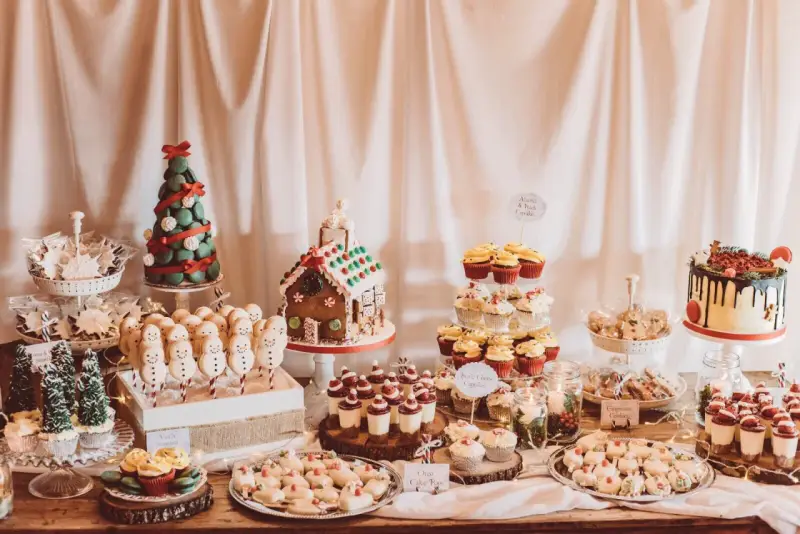 Mesa llena de postres navideños: árbol de macarons, casa de jengibre, muñecos de nieve, cupcakes y galletas.
