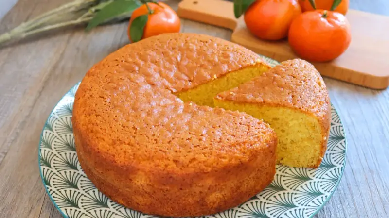 Bizcocho de mandarina y yogur, esponjoso y dorado, con una porción cortada. Mandarinas frescas al fondo.